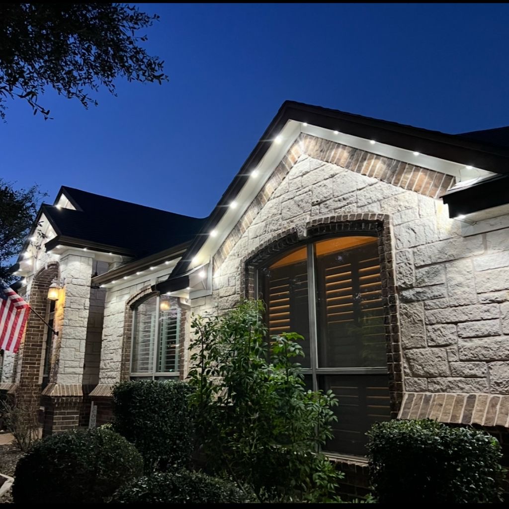 Cool-white permanent fascia puck lighting on a stone-and-brick home at dusk